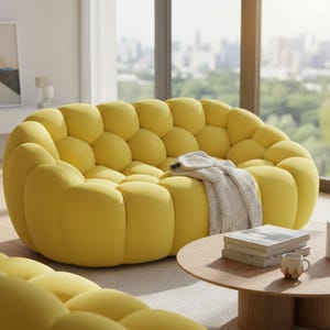 May include: A modern, yellow bubble sofa with a round shape. A light gray blanket rests on the sofa. A round wooden coffee table holds books and a mug. The sofa is in a bright, sunlit room with a view of a city.