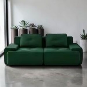 Puede incluir: Un sof&aacute; moderno de color verde esmeralda con un dise&ntilde;o minimalista. El sof&aacute; tiene dos cojines grandes para el asiento y dos cojines para el respaldo, con reposabrazos a ambos lados. Est&aacute; colocado frente a una pared blanca y un suelo de hormig&oacute;n.