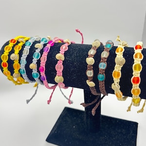 Puede incluir: Una muestra de pulseras de cuentas coloridas con varios colores, incluyendo amarillo, naranja, rosa, azul y verde. Las pulseras están hechas con pequeñas cuentas de vidrio y están atadas con cuerda.