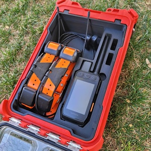 May include: A red hard case with a black interior holds a Garmin GPS device and two orange and black dog collars. The collars have the word "Garmin" printed on them.
