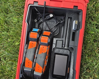 May include: A red hard-shell carrying case containing two orange and black Garmin tracking collars, a black handheld GPS device with an antenna, a black charging cable, and a small rectangular component, all organized within a custom-molded interior.