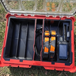 May include: Open red and black Milwaukee Packout storage case with a clear lid. Inside are black compartments, orange dog collars, and a GPS device. The case is on a grassy surface.