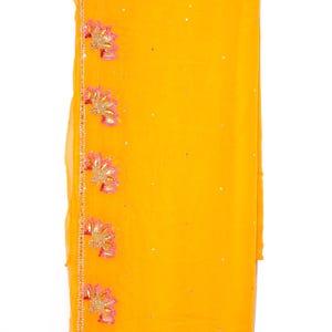 May include: A yellow sheer scarf with pink and gold embroidery. The scarf has a beaded trim and tassels.