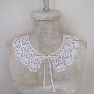 May include: White crocheted collar with a bow tie. The collar is made of delicate lace and has a scalloped edge.