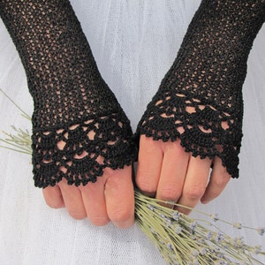 May include: A pair of black fingerless gloves featuring an intricate openwork crochet pattern throughout the length and a decorative scalloped lace-like border at the wrist, crafted with fine black thread in a delicate, airy, and textured design.
