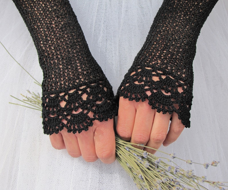 May include: A pair of black fingerless gloves featuring an intricate openwork crochet pattern throughout the length and a decorative scalloped lace-like border at the wrist, crafted with fine black thread in a delicate, airy, and textured design.