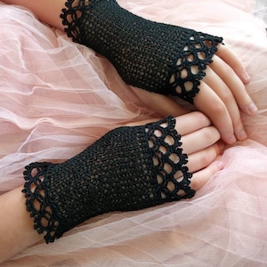 May include: Black crochet fingerless gloves with a scalloped edge. The gloves are made of a fine, open weave and are displayed on a pink tulle background. The gloves are a stylish accessory.