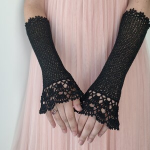 May include: A pair of black fingerless gloves crafted from fine crochet thread. The gloves extend from the mid-forearm to the knuckles, featuring a delicate, intricate lace pattern at the flared cuffs and a simple, tight-knit stitch throughout.