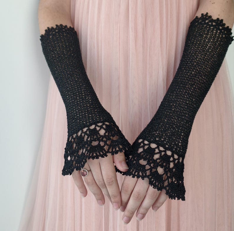 May include: A pair of black fingerless gloves crafted from fine crochet thread. The gloves extend from the mid-forearm to the knuckles, featuring a delicate, intricate lace pattern at the flared cuffs and a simple, tight-knit stitch throughout.