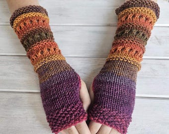 May include: A pair of hand-knitted fingerless gloves in shades of purple, orange, and brown. The gloves feature a textured knit pattern with openwork details near the wrist. The color gradient transitions from deep purple to orange and brown.