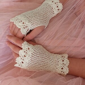 May include: A pair of off-white fingerless gloves featuring a delicate crochet knit pattern. The gloves have a scalloped edge design at both the wrist and the finger openings, crafted with a fine thread to create a lightweight, openwork texture.