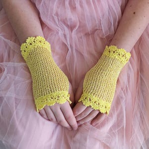 May include: A pair of bright yellow fingerless gloves featuring a delicate, open-knit texture and intricate scalloped crochet trim at both the top and bottom edges. The gloves are crafted with a fine yarn, providing a lightweight appearance.