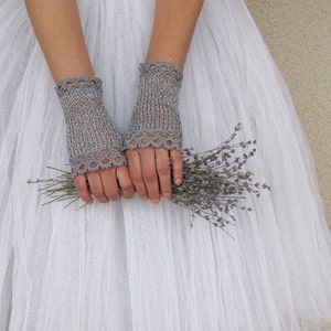 May include: A pair of gray fingerless gloves with a delicate lace trim. The gloves are knitted and held together with a bouquet of dried lavender. The gloves are a light gray color and are made of a soft, textured material.