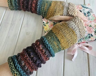 May include: Hand-knitted fingerless gloves in a mix of colors including teal, brown, and yellow. The gloves are made of a soft, textured yarn and feature a ribbed cuff and a patterned design on the arm. A floral patterned book is in the background.