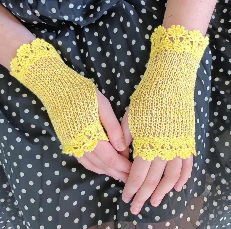 May include: A pair of bright yellow fingerless gloves featuring a delicate, intricate crochet lace trim at both the top and bottom edges. The main body of the gloves is crafted from a fine, lightweight knit fabric with a subtle, semi-sheer texture.