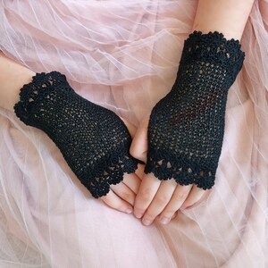 May include: A pair of black fingerless gloves featuring a fine crochet mesh pattern throughout the main body and a decorative scalloped lace edge at both the wrist and the knuckle openings, crafted with a delicate and intricate thread design.