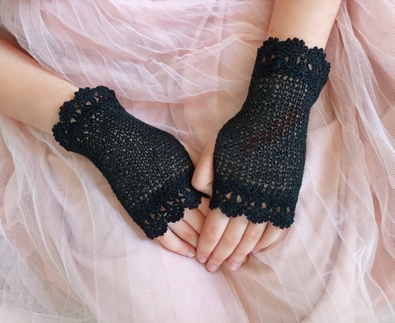 May include: A pair of black fingerless gloves featuring a fine crochet mesh pattern throughout the main body and a decorative scalloped lace edge at both the wrist and the knuckle openings, crafted with a delicate and intricate thread design.