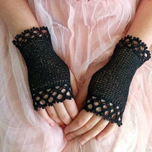 May include: A pair of black fingerless gloves. The gloves are made of a delicate, open-weave material. The cuffs and the top edge of the gloves are adorned with a scalloped, lace-like trim. The gloves are designed to cover the hand up to the knuckles.
