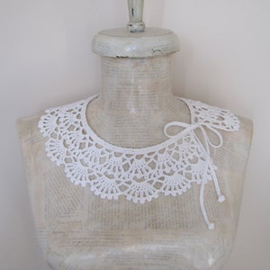 May include: White crocheted collar with a delicate lace pattern. The collar is tied at the back with a white ribbon.