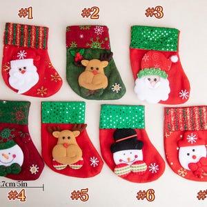 K&ouml;nnte beinhalten: Sieben Weihnachtsstr&uuml;mpfe, nummeriert von 1 bis 7, mit einer Gr&ouml;&szlig;e von jeweils 15,8 cm mal 12,7 cm. Die Str&uuml;mpfe zeigen festliche Motive wie den Weihnachtsmann, Rentiere und Schneem&auml;nner, verziert mit rotem und gr&uuml;nem Stoff, Glitzer und Schneeflocken.