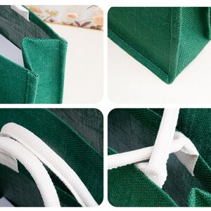K&ouml;nnte beinhalten: Eine dunkelgr&uuml;ne Tragetasche aus strukturiertem Webstoff. Die Tasche verf&uuml;gt &uuml;ber einen quadratischen Boden, verst&auml;rkte Seitenteile und zwei dicke, wei&szlig;e geflochtene Seilgriffe, die mit wei&szlig;en Stofflaschen an den oberen Kanten befestigt sind.