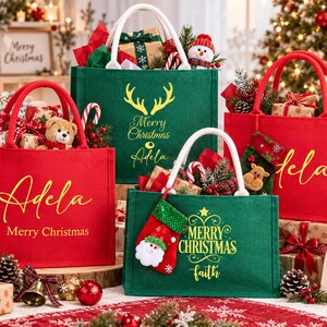 K&ouml;nnte beinhalten: Vier rechteckige Jute-Tragetaschen in Rot und Gr&uuml;n mit wei&szlig;en Henkeln. Die Taschen sind mit goldenem Text personalisiert, darunter Namen wie Adela und Faith sowie Schriftz&uuml;ge wie Merry Christmas, und mit festlichen Weihnachtsmotiven verziert.