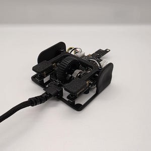May include: A black and gray computer mouse with exposed internal components. The mouse has a black braided cable and a central wheel. The design features a combination of plastic and metal parts, showcasing the internal circuitry.