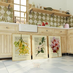 Może przedstawiać: Trzy oprawione grafiki botaniczne z ilustracjami kwiatowymi. Grafiki przedstawiają nazwy "Ylang-Ylang", "Sampaguita" i "Waling-Waling" z tekstem w języku obcym. Grafiki są wystawione w otoczeniu kuchni z drewnianymi szafkami i podłogą z kafelkami w szachownicę.