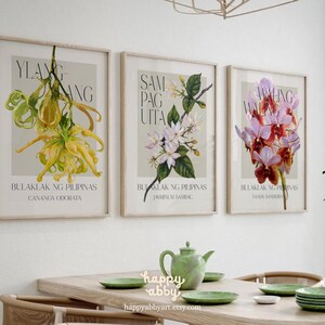 Może przedstawiać: Trzy oprawione grafiki botaniczne z ilustracjami kwiatowymi. Grafiki przedstawiają ż&oacute;łte, białe i fioletowe kwiaty, każda z tekstem w obcym języku. Grafiki są wyświetlane nad drewnianym stołem z zielonymi talerzami i imbrykiem.