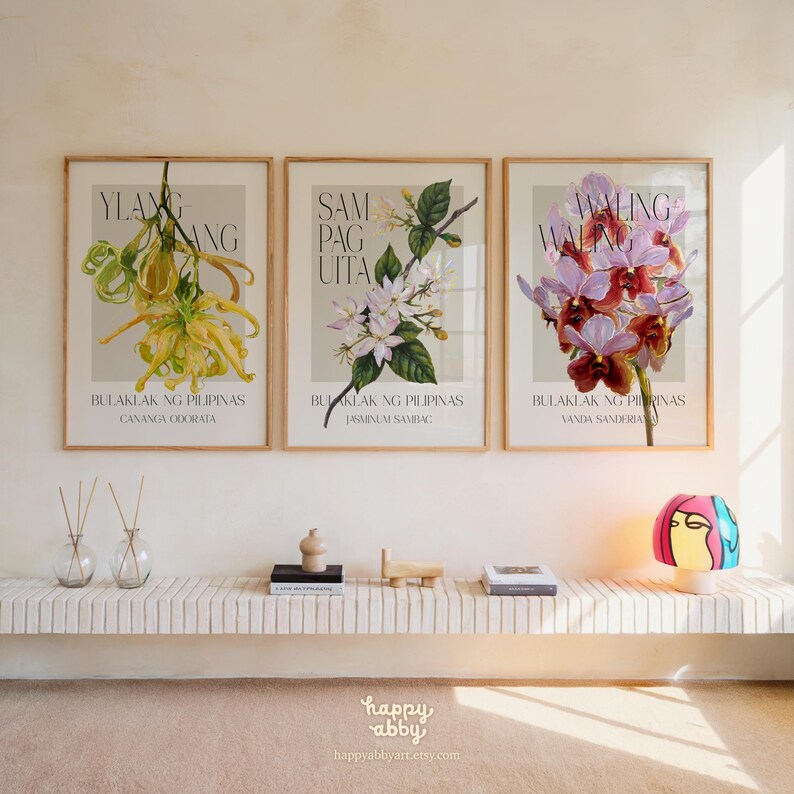 Może przedstawiać: Trzy oprawione grafiki botaniczne z ilustracjami kwiat&oacute;w. Grafiki przedstawiają ż&oacute;łte, białe i fioletowe kwiaty z tekstem w stylizowanej czcionce. Każda grafika zawiera naukową nazwę kwiatu. Grafiki są eksponowane nad p&oacute;łką z elementami dekoracyjnymi.