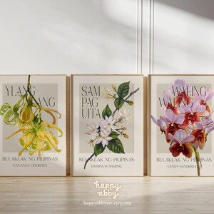 Może przedstawiać: Trzy oprawione botaniczne wydruki artystyczne z ilustracjami kwiatowymi. Wydruki przedstawiają ż&oacute;łte ylang-ylang, białe sampaguita i fioletowe kwiaty waling-waling. Każdy wydruk zawiera tekst w języku angielskim i tagalog.