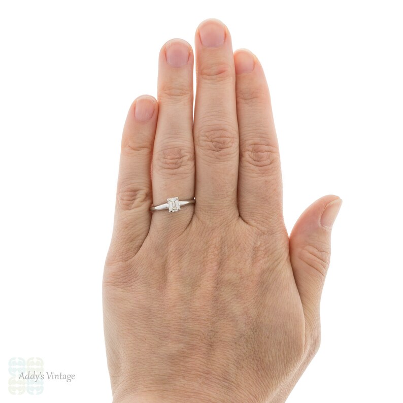 May include: A silver ring with a square-shaped emerald cut diamond.