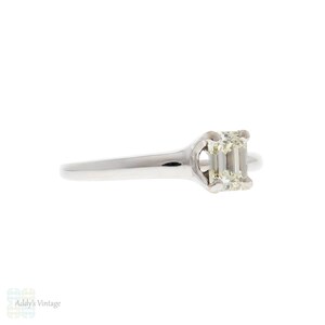 May include: A silver ring with a single emerald-cut diamond set in a simple, elegant design.