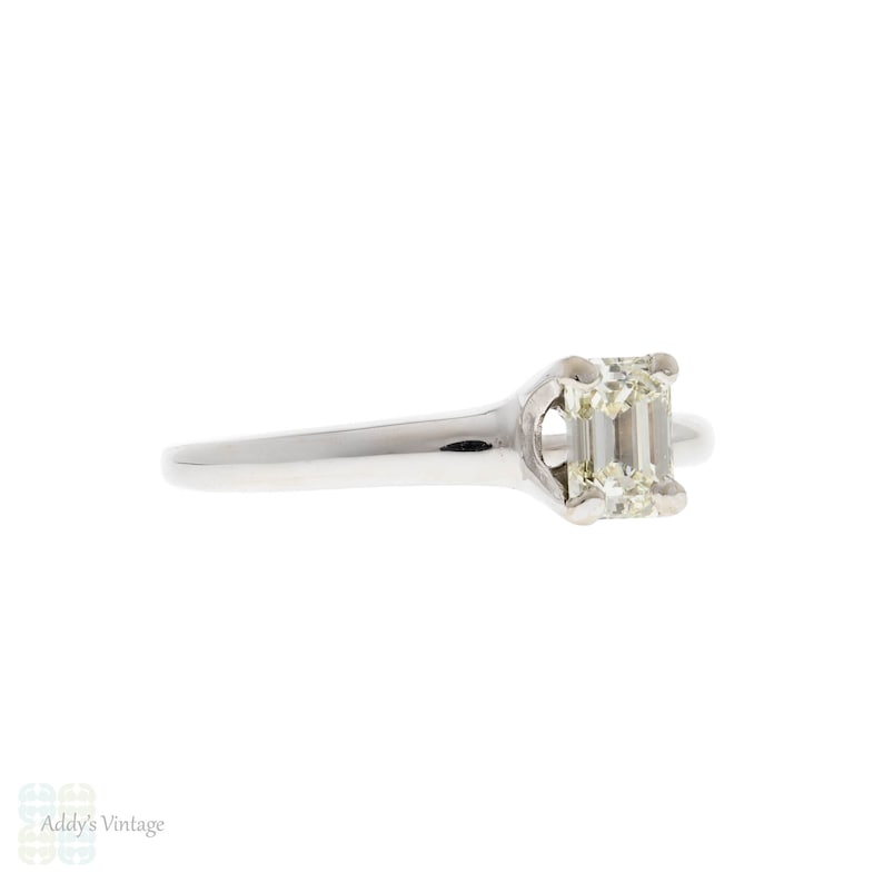 May include: A silver ring with a single emerald-cut diamond set in a simple, elegant design.