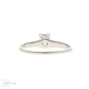 May include: A simple solitaire engagement ring with a single, round, prong-set diamond. The ring is made of white gold and has a polished finish.
