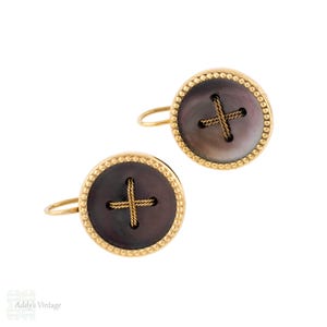 May include: A pair of gold-toned button earrings. Each earring features a dark gray, circular center with a gold cross design and a gold beaded border. The earrings have a simple, curved gold hook.