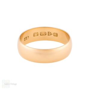 May include: A gold-colored ring with a smooth, rounded band. The ring has several small markings stamped on the exterior. The ring is likely made of gold and is a classic style.