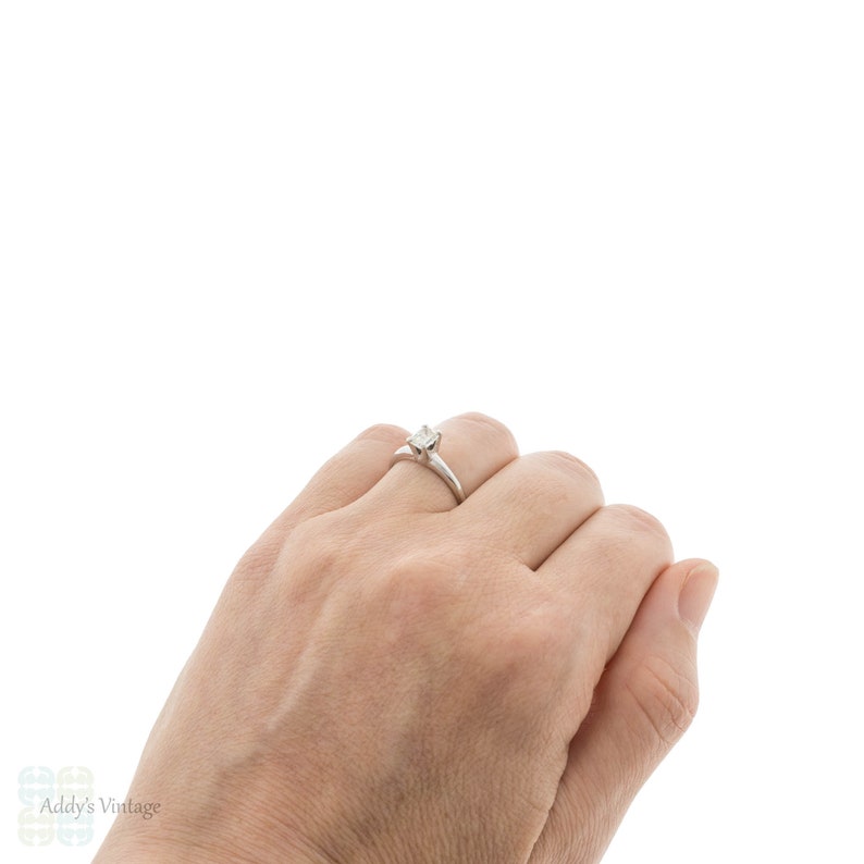 May include: A simple silver band ring with a single, clear, round diamond set in the center.