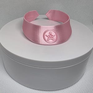 Op de afbeelding: Een roze satijnen choker met een stervormig ontwerp in het midden.