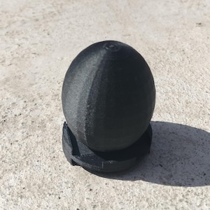 May include: A black 3D printed egg on a black base.