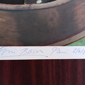 May include: A framed artwork featuring a brown, bowl-shaped object with a white rim, set against a green and brown background. The artist's signature and the date 2/4/86 are visible in blue ink.
