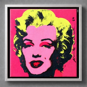 May include: Pop art portrait of Marilyn Monroe in a square, silver-framed canvas. The artwork features a vibrant color palette with a pink background, a pink face, and yellow hair. The lips are red, and the eyes are accented with red eyeshadow.
