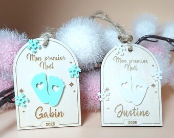 May include: Two wooden Christmas ornaments with the text "Mon premier Noël" and baby footprints. One ornament says "Gabin" and the other says "Justine", both with the year 2025. The ornaments are decorated with snowflakes.