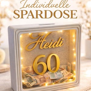 May include: A white shadow box with the name "Heidi" and the number "60" in gold lettering. The box is filled with money and illuminated by small lights. The text "Individuelle SPARDOSE" is at the top.