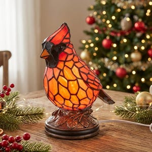 May include: A stained glass lamp shaped like a cardinal bird with red and orange glass panels, a black face, and a brown textured base. The lamp is illuminated and features a power cord. The text www.nameandcharm.etsy.com is visible at the bottom.