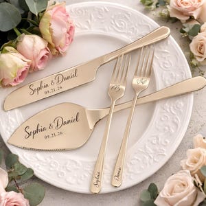 Peut inclure: Un ensemble de service à gâteau de mariage doré, comprenant un couteau et une pelle à gâteau gravés des noms "Sophia & Daniel" et la date "09.21.26". Deux fourchettes sont également incluses, avec les noms "Sophia" et "Dania" gravés.