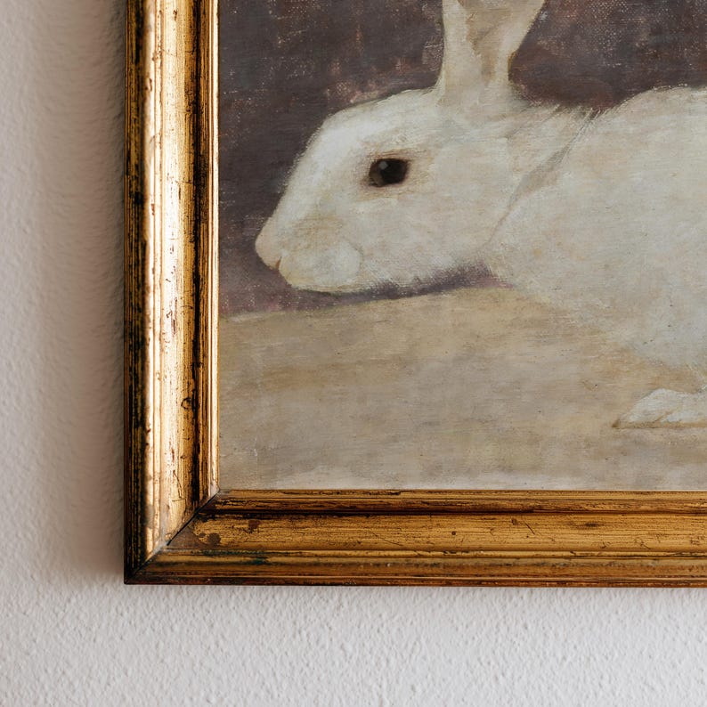 Puede incluir: Pintura enmarcada de un conejo blanco en un marco dorado. El conejo est&aacute; representado de perfil, con un aspecto suave y texturizado. El fondo es un tono apagado y terroso, que realza el pelaje blanco brillante del conejo.