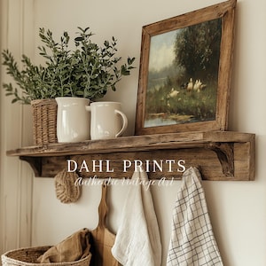May include: A rustic wooden wall shelf featuring a framed landscape painting of ducks in a field, two white ceramic pitchers, a wicker basket with greenery, and hanging kitchen textiles. The text DAHL PRINTS Authentic Vintage Art is visible.