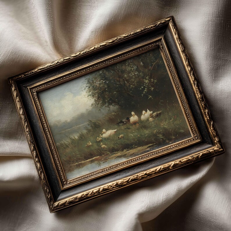 May include: A rectangular framed painting featuring a landscape scene with several white ducks and ducklings near a body of water and trees. The frame is black with ornate gold-colored detailing along the inner and outer edges of the border.