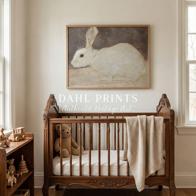 Puede incluir: Una impresi&oacute;n art&iacute;stica vintage enmarcada de un conejo blanco cuelga sobre una cuna de madera. La cuna tiene un oso de peluche y una manta beige. El texto "DAHL PRINTS Authentic Vintage Art" est&aacute; debajo.